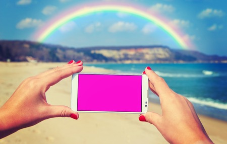 White smart phone on the background Black Sea in female hands and rainbowの写真素材