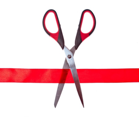 Scissors cutting through red ribbon or tape, isolated on whiteの写真素材