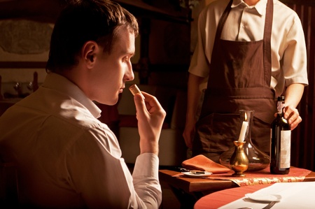 Young man sniffing the cork of a wine bottle