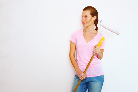 Happy woman with roller brush standing against wall.