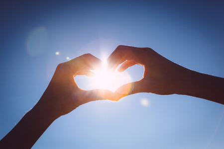 Hands making love shape sign on bright blue sky.の写真素材