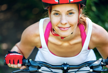 Happy Young woman leaned over the handlebars of her bike.の写真素材