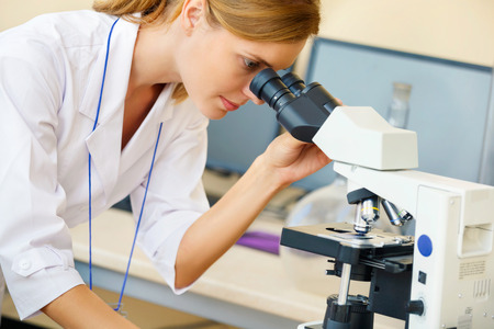 Beautiful woman in a laboratory working with a microscope.