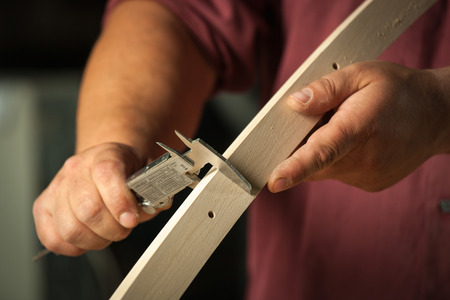 Carpenter measuring chair part with electric callipers in workshop.の写真素材