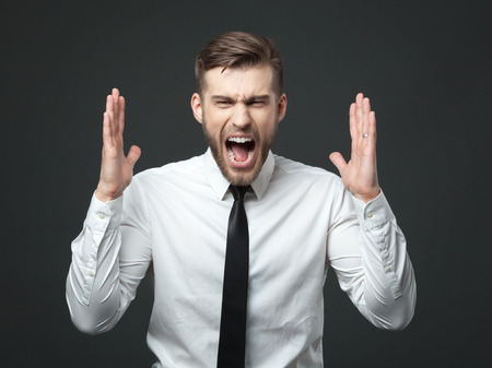 Why! Young businessman screaming at camera isolated on dark gray backgroundの写真素材