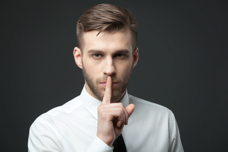 Keep your secrets! Studio portrait of young handsome businessman gesturing "shh" to the camera.の写真素材