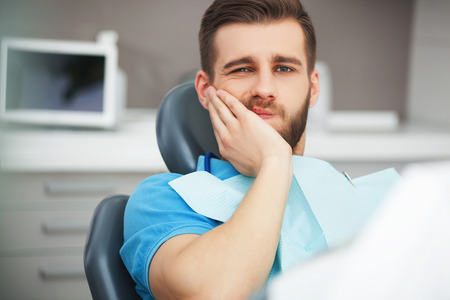 Shot of a young man with tooth pain while sitting in a dentist's chair.の写真素材