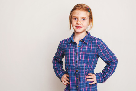 Portrait of little redhead girl in blue plaid shirt posing against wall.の写真素材