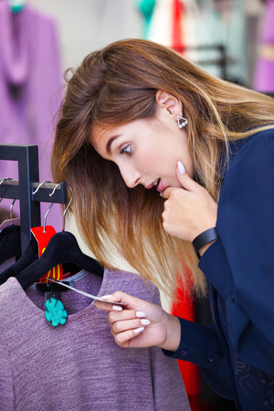 Young woman shocked by the price while looking at some clothing in a store.の写真素材
