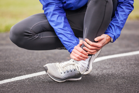 Cropped shot of a young man holding his ankle in pain while running.の写真素材