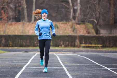 Full lenght shot of a young woman running on a stadium.