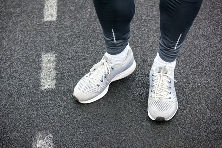 Legs in gray colored running shoes standing on asphalt.