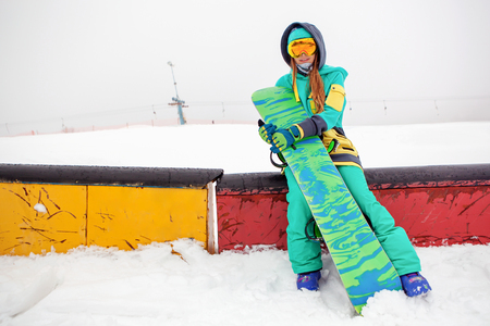 Portrait of beautiful happy young snowboarder with her snowboard.の写真素材