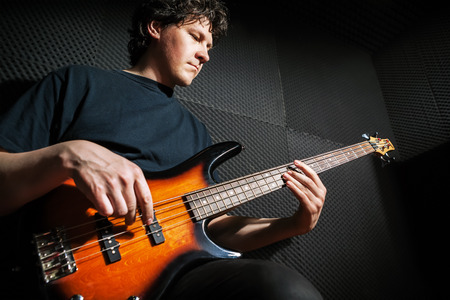 Handsome rock bass guitarist practicing in sound studio.の写真素材