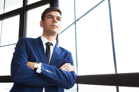 Portrait of young handsome businessman leaning against window with his arms crossed.の写真素材