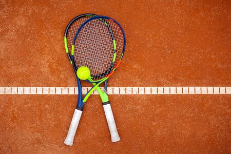 Top view of two tennis rackets and yellow tennis ball lie on the clay court close up.