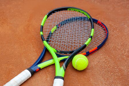 Two tennis rackets and yellow tennis ball lie on the clay court close up.