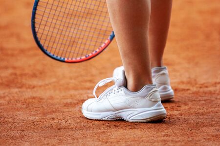 Female tennis player legs in tennis shoes standing on a clay court close up.の写真素材
