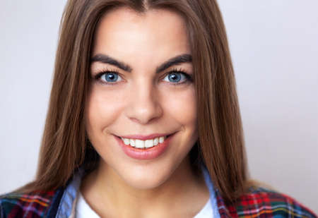 Studio portrait of happy young woman in plaid shirt posing against wall.