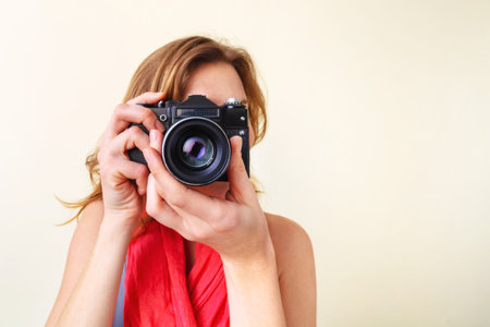 Young redhead woman looking through viewfinder with an old 35mm slr camera.の写真素材