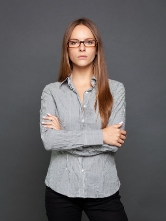 Studio portrait of a beautiful confident young woman in eyeglasses posing with crossed hands.の写真素材