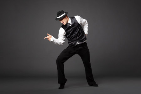 Confident young man dancing in gangster style suite. Studio shot isolated on gray background.の写真素材