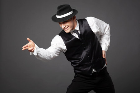 Confident young man dancing in gangster style suite. Studio shot isolated on gray background.の写真素材