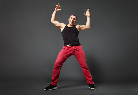 Full body portrait of young man dancing against gray background. Low and Wide angled view effect.の写真素材