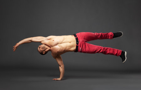 Young male professional dancer B-boying in studio isolated on gray background.の写真素材
