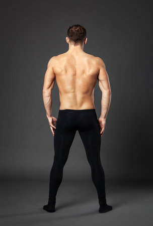 Full-length portrait of a young ballet dancer photographed from behind, standing in front of a gray background.の写真素材