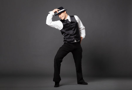 Confident young man dancing in gangster style suite. Studio shot isolated on gray background.の写真素材