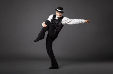 Confident young man dancing in gangster style suite. Studio shot isolated on gray background.の写真素材