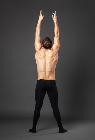 Portrait of a young ballet dancer photographed from behind, standing with raised hands in front of a gray background.の写真素材
