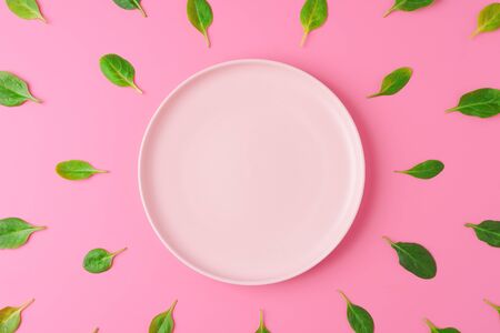 Spinach leaves around empty plate on pink background. Green healthy eating creative concept. Top view, copy spaceの写真素材