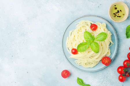 Italian food - spaghetti pasta decorated with cherry tomatoes, olive oil, basil and spices on grey blue background, copy space, flat layの写真素材