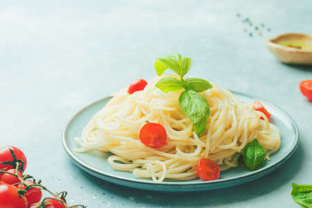 Italian food - spaghetti pasta decorated with cherry tomatoes, olive oil, basil and spices on grey blue background, copy space, closeupの写真素材