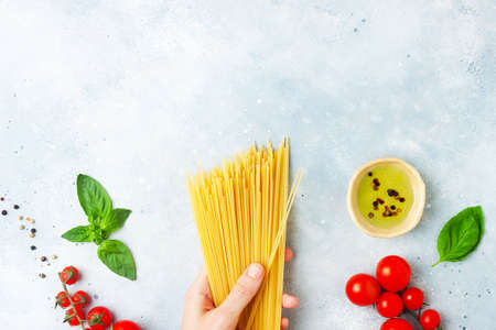 Italian food - female hand holding raw spaghetti: pasta ingredients concept on grey stone background, copy space, flat layの写真素材