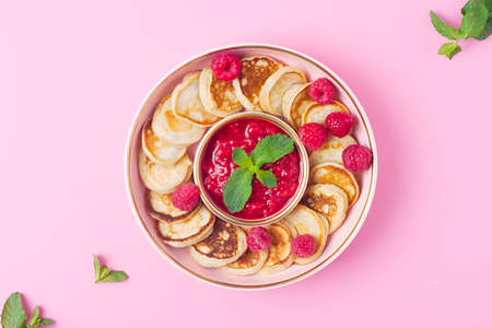 Trendy food - mini pancakes cereal. Heap of mini cereal pancakes with raspberry jam in bowl on pink background. Copy space. Top view or flat lay.の写真素材