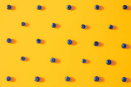 Seamless pattern with fresh sweet blueberry fruit on colorful yellow background. Dessert healthy food concept. Raw summer diet. Delicious nature vegetarian ingredient. Flat lay, minimal styleの写真素材