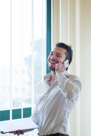 business man talking on a cellphone  in a office, in front of the windowの写真素材