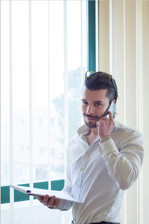 business man talking on a cellphone  in a office, in front of the windowの写真素材