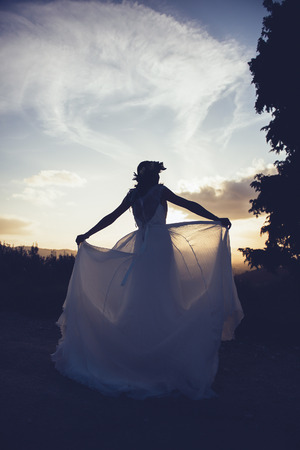 silhouette of bride in a landscape, with wedding dress moved by the windの写真素材