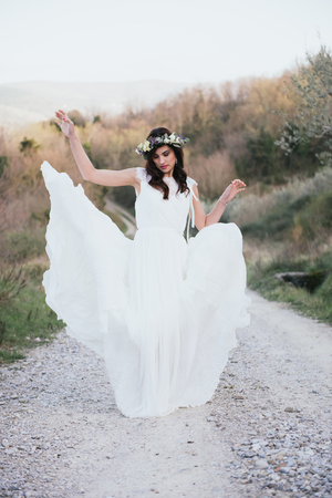 portrait of bohemian and hippie bride in countryside, with wedding dress moved by the windの写真素材