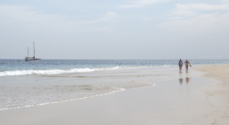 A couple walking on the beach  A sailboat anchored nearの写真素材
