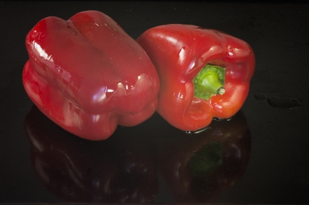 Two red peppers soaked in oil, ready to be tucked into the oven and roast  They are on a black background with a few drops of oilの写真素材
