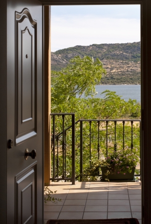 Can see the open door of a home with a balcony and a lake in the background. It is a house in a rural environment and transmits tranquility and peace.の写真素材