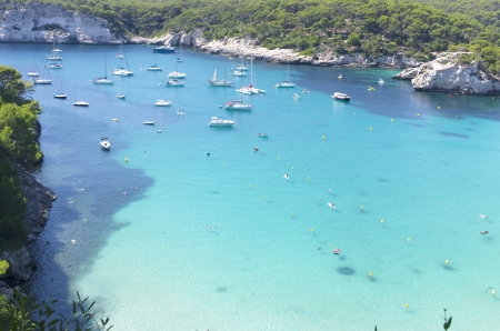 Cala in Menorca, Mediterranean sea  There are unknown people bathing, swimming or snorkeling  There are some sailboats, powerboats or yachts anchoredの写真素材