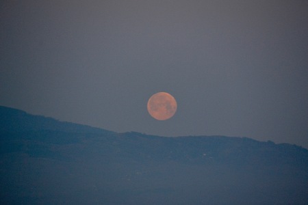A full moon sinking from view behind the Pirin Mountains outside of Melnik, Bulgaria as dawn approachesの写真素材