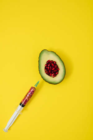 Flat lay concept avocado sliced with seed of pomegranate red color with Christmas vaccine full of glitter on yellow backgroundの写真素材