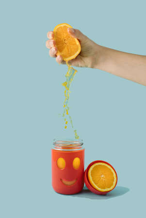 Healthy real life composition. Woman hand squeeze orange. Making organic fresh juice in smiling happy jar or cup. colored background with half fruit.の写真素材